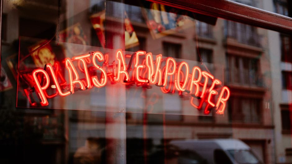 Enseigne néon rouge 'Plats à Emporter' reflétée dans la fenêtre d'une ville, ambiance urbaine.