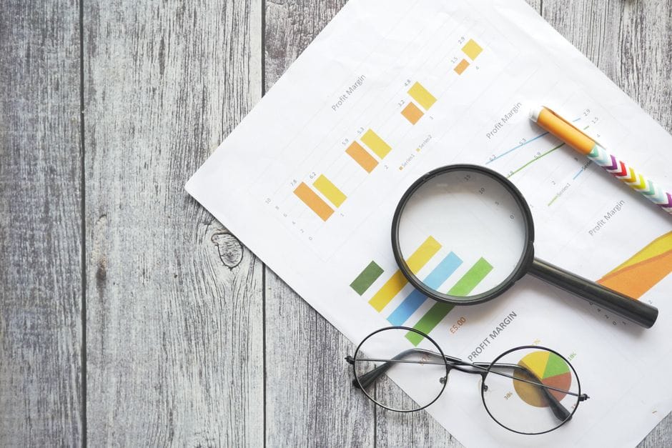 Vue de dessus des graphiques financiers, une loupe, un stylo à bille et des lunettes sur une surface en bois.