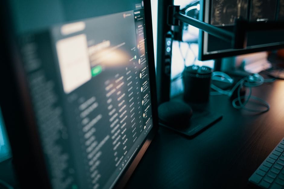Espace de travail élégant avec des écrans doubles dans une pièce faiblement éclairée, idéal pour la productivité et les passionnés de technologie.