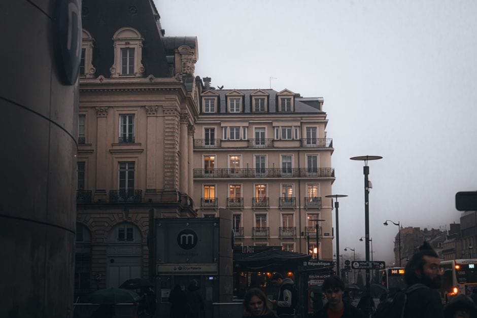 Vue de rue brumeuse en soirée avec une architecture classique et une vie urbaine animée.