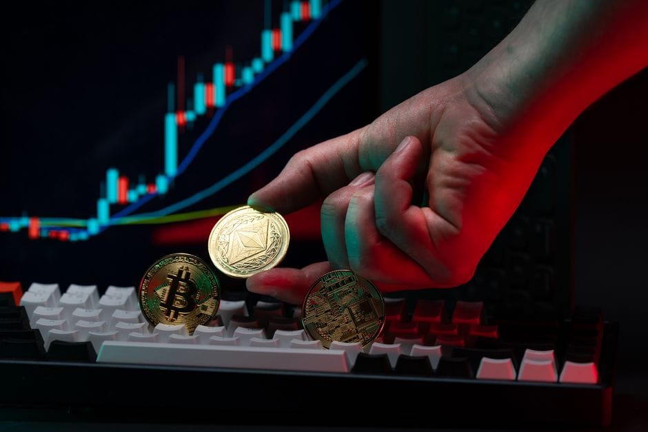 Gros plan d'une main tenant des pièces de crypto-monnaie sur un clavier, avec un affichage graphique en arrière-plan.