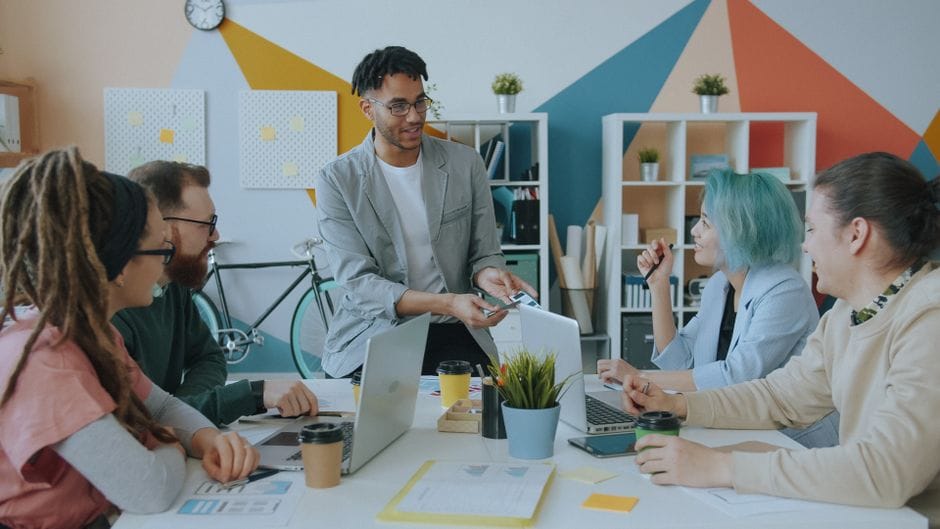 Une équipe diversifiée collabore dans un bureau moderne, échangeant des idées avec des ordinateurs portables et du café.