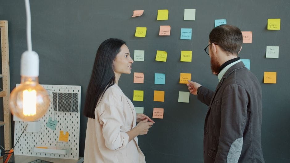 Deux professionnels échangent des idées à l'aide de post-it colorés sur un tableau noir.