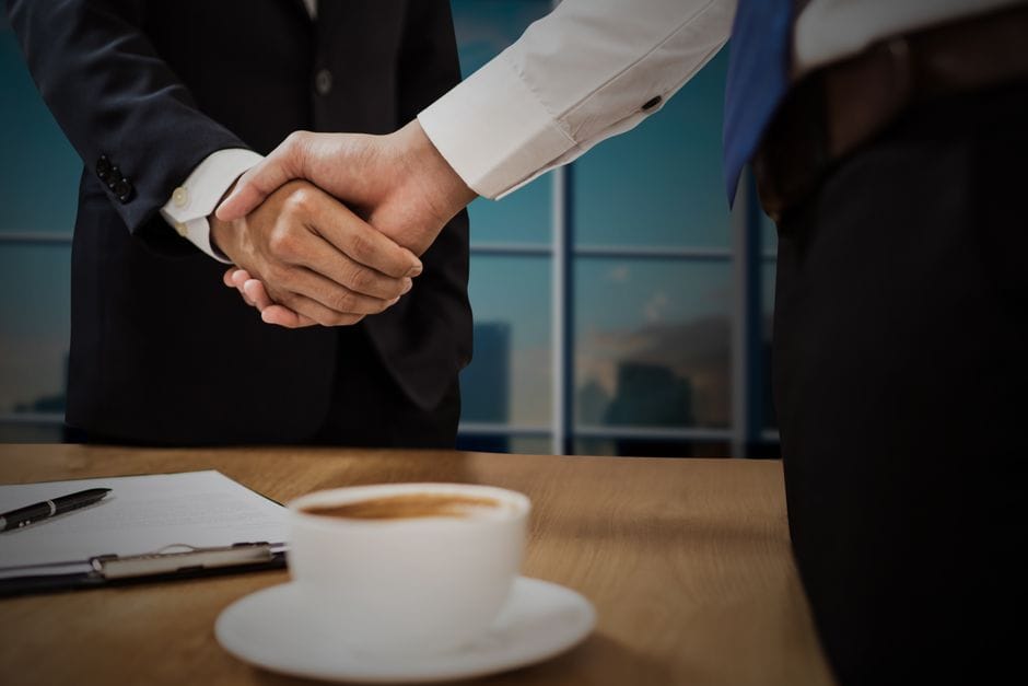 Deux professionnels se serrant la main au-dessus d'un bureau avec une ville en arrière-plan.