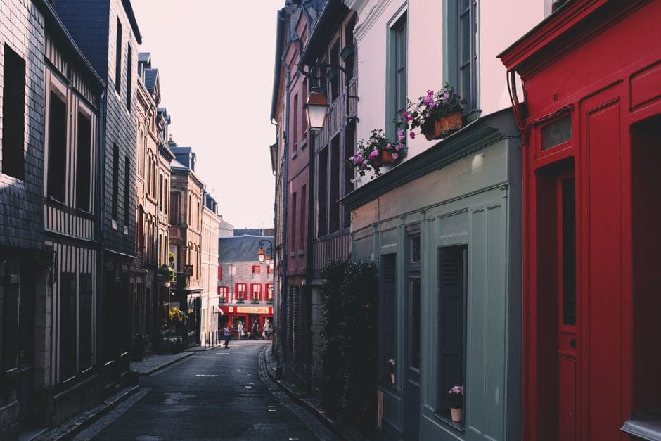 Une rue étroite pittoresque bordée de maisons colorées et de jardinières fleuries dans une ville européenne.