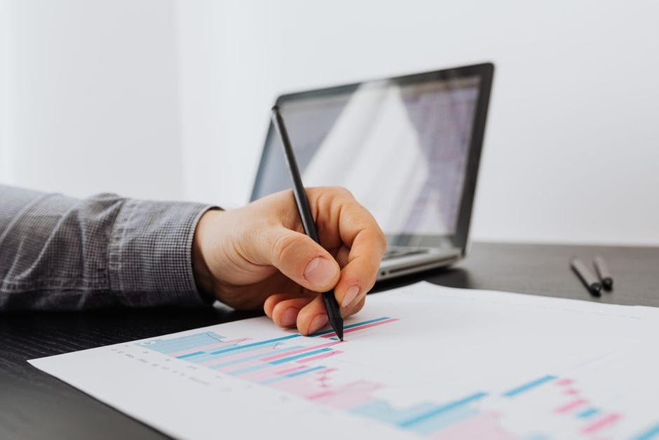 Personne prenant des notes sur un graphique d'affaires avec un ordinateur portable en arrière-plan.
