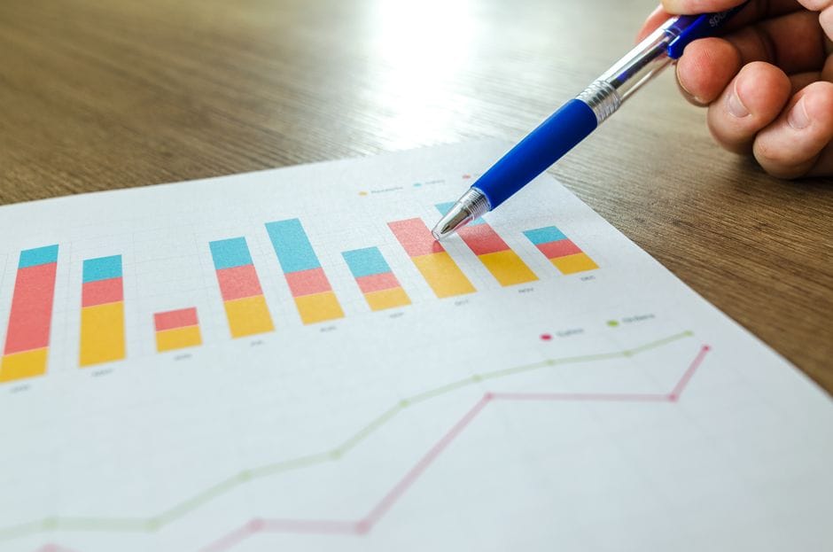 Gros plan détaillé d'une main pointant vers des graphiques colorés avec un stylo bleu sur une surface en bois.