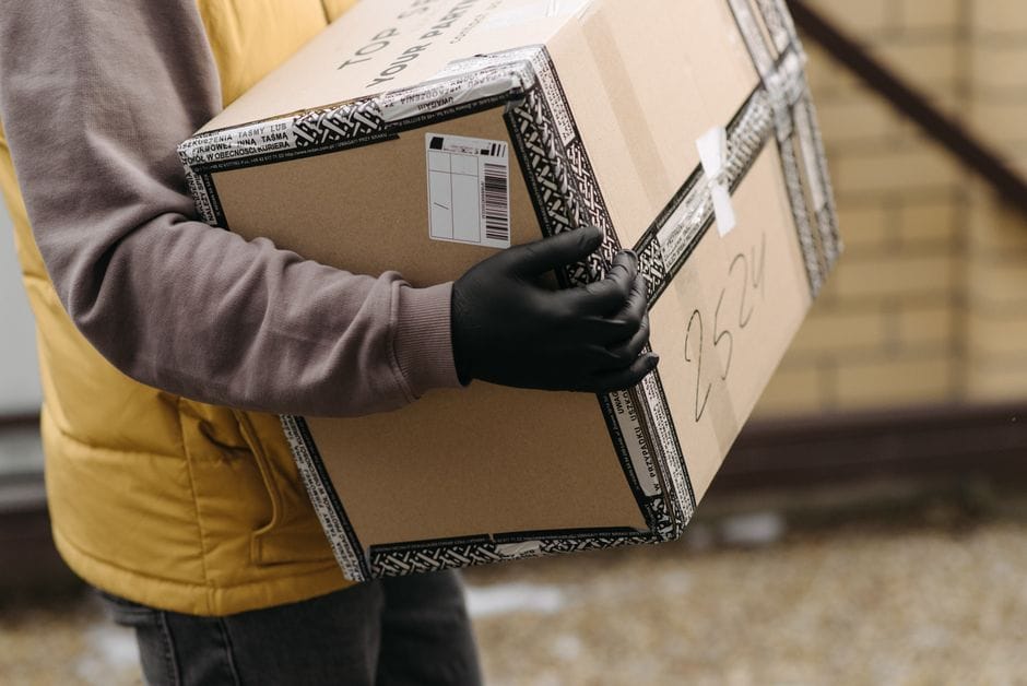 Coursier tenant un colis marqué 'TOP PACKAGING' portant des gants pour une livraison sécurisée.