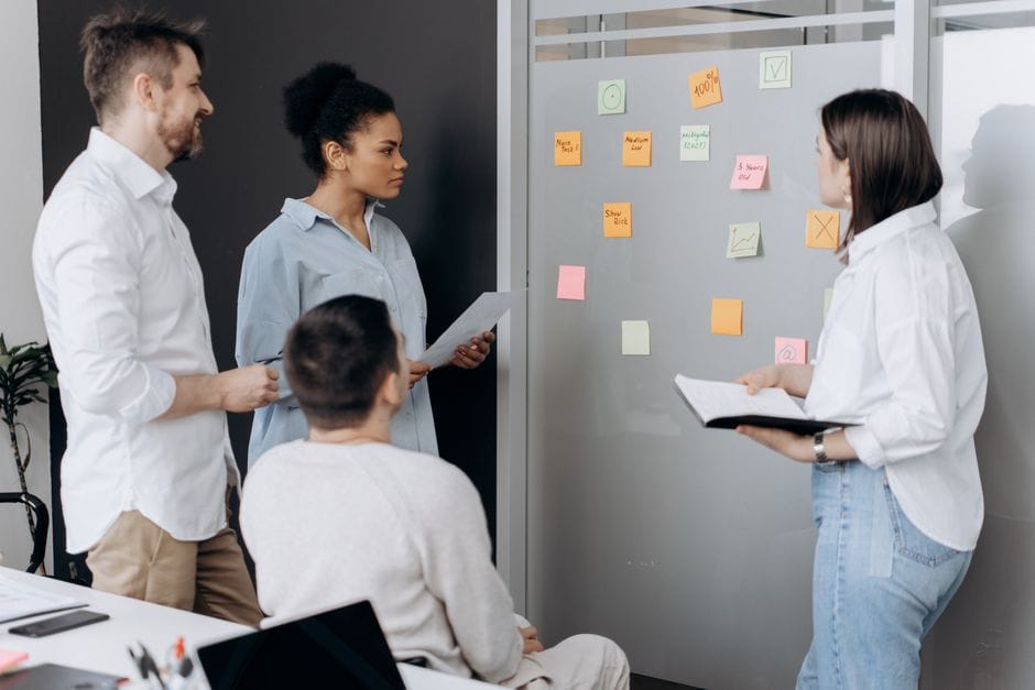 Équipe diversifiée collaborant dans un bureau, discutant des idées en utilisant des post-it et des carnets.