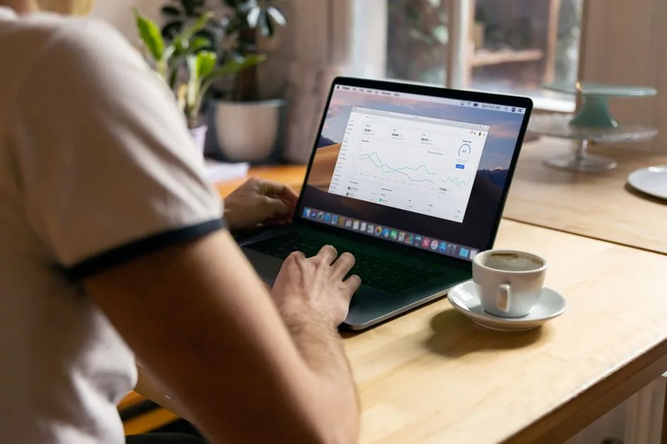 Personne travaillant sur un ordinateur portable avec des analyses dans un bureau à domicile confortable, café à la main.