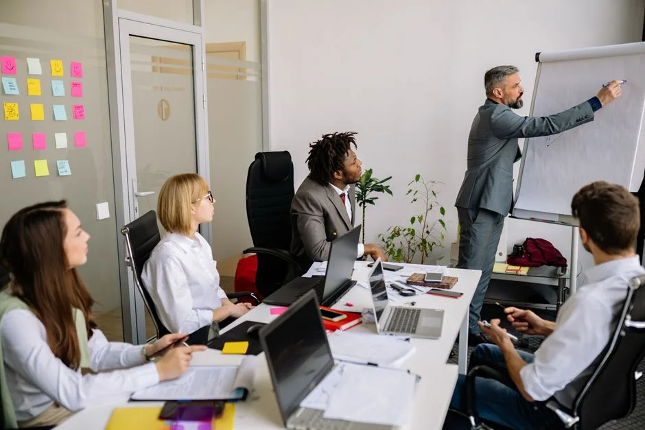 Équipe d'affaires engagée dans une réunion collaborative avec un leader présentant sur un tableau flottant.