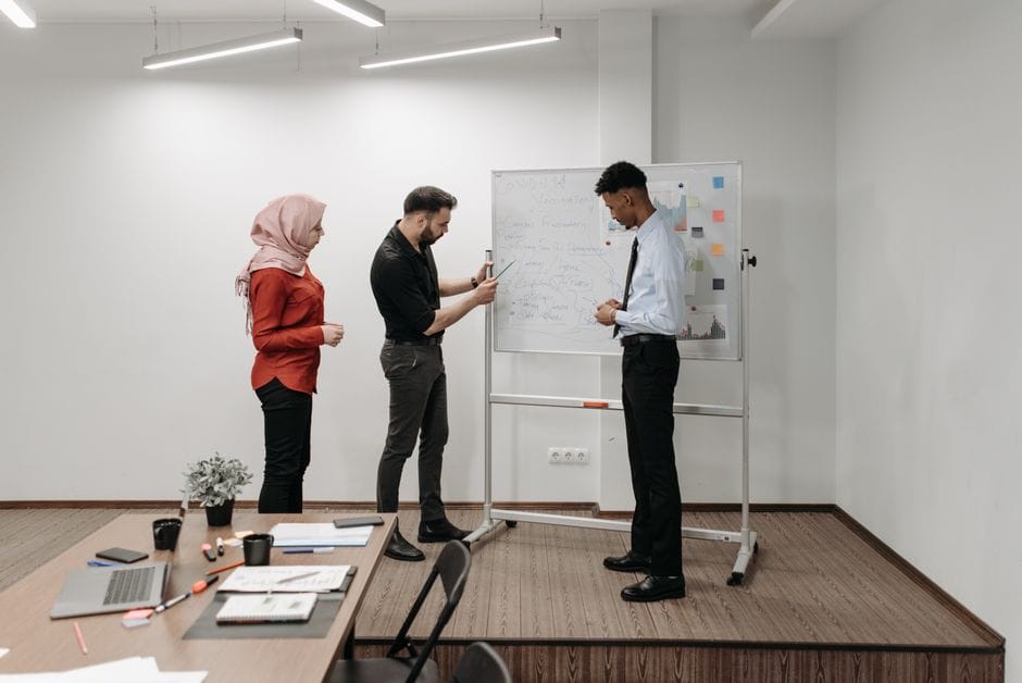Trois professionnels discutant d'idées de projet lors d'une réunion de bureau, illustrant le travail d'équipe et la diversité.