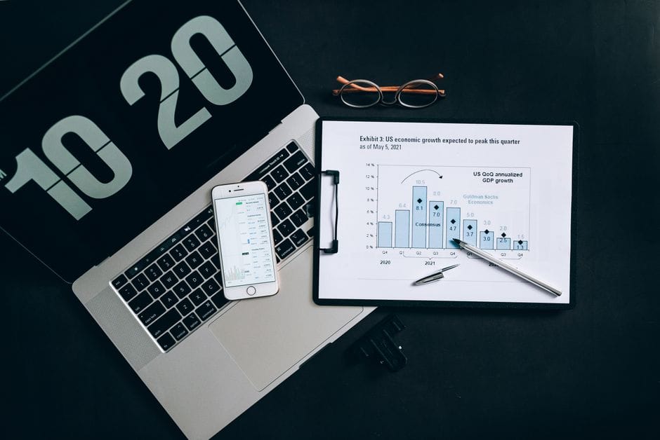 Vue de dessus des outils d'analyse financière sur un bureau, incluant un ordinateur portable, un smartphone et des graphiques.