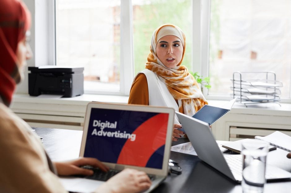 Deux femmes en hijabs discutent de la publicité numérique dans un cadre de bureau.