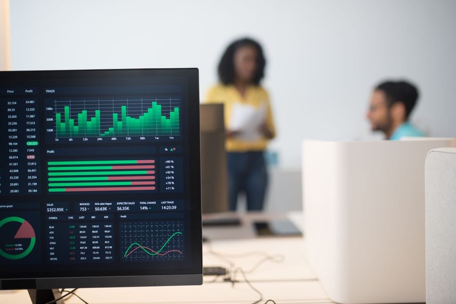 Bureau moderne avec des écrans de trading financier et une équipe diversifiée discutant des stratégies.