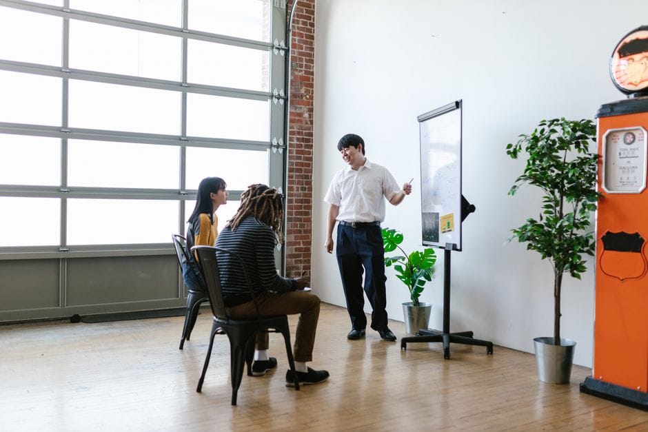 Une réunion dans un bureau moderne avec un présentateur expliquant des concepts sur un tableau blanc.
