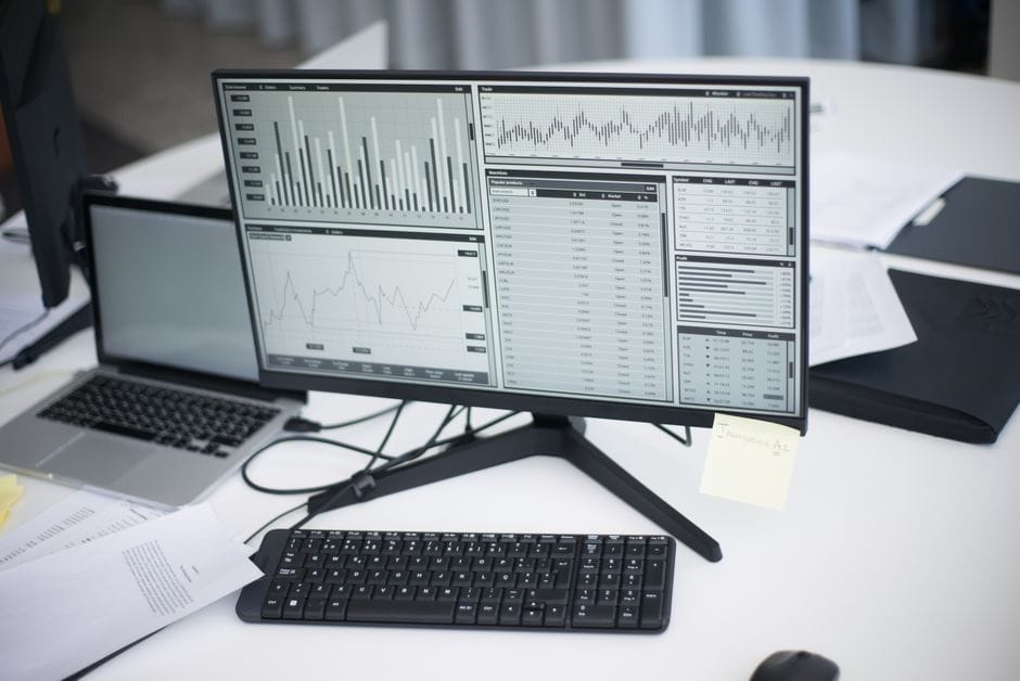 Un espace de travail professionnel avec des ordinateurs et des graphiques analytiques sur un moniteur, symbolisant un environnement d'affaires moderne.